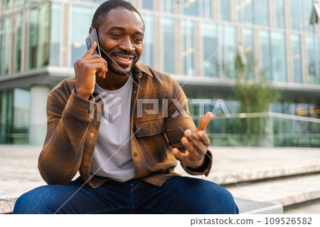 African american man talking on smartphone on street in city outdoor. Man with cell phone chatting with friends. Smiling person making answering call by cellphone. Guy having conversation by mobile African american man talking on smartphone on street in city outdoor. Man with cell phone chatting with friends. Smiling person making answering call by cellphone. Guy having conversation by mobile 109526582