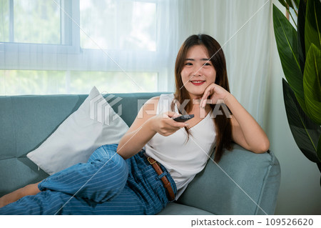 Beautiful female person look movie holding remote controller watching television, woman smiling sit relaxing watch TV hold remote control looking news on sofa in living room, entertainment lifestyles Beautiful female person look movie holding remote controller watching television, woman smiling sit relaxing watch TV hold remote control looking news on sofa in living room, entertainment lifestyles 109526620
