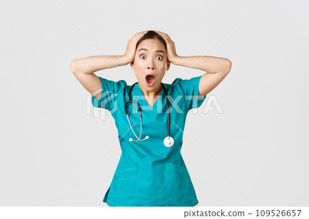 Covid-19, healthcare workers and preventing virus concept. Shocked and anxious asian female doctor in panic, grab head and screaming alarmed, have big problem, got in trouble, white background 109526657