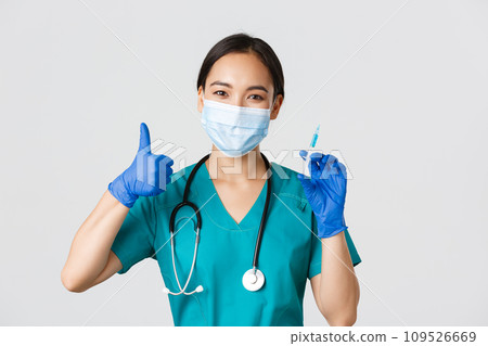Covid-19, coronavirus disease, healthcare workers concept. Smiling beautiful asian medical worker, nurse in mask and gloves thumb-up, hold syringe with vaccine, standing white background Covid-19, coronavirus disease, healthcare workers concept. Smiling beautiful asian medical worker, nurse in mask and gloves thumb-up, hold syringe with vaccine, standing white background 109526669