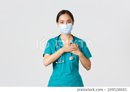 Covid-19, coronavirus disease, healthcare workers concept. Friendly caring asian female doctor, physician in medical mask and gloves, holding hands on heart and smiling, white background 109526681