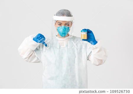 Covid-19, coronavirus disease, healthcare workers concept. Side view of serious tech lab employee, researcher in personal protective equipment show thumb-down in disapproval, bad analyze result 109526730