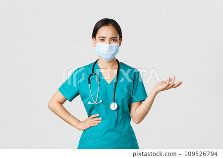 Covid-19, coronavirus disease, healthcare workers concept. Confused and upset asian female doctor in medical mask and scrubs, raise hand up puzzled, cant understand what problem, white background 109526794