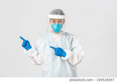 Covid-19, coronavirus disease, healthcare workers concept. Surprised female asian doctor, physician in medical respirator and personal protective equipment pointing upper left corner 109526847