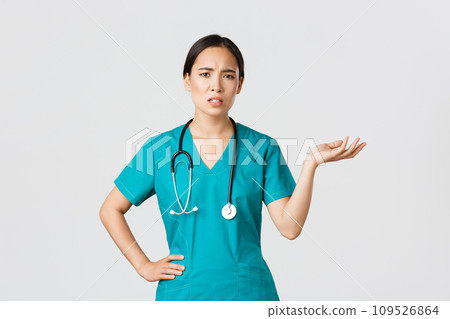 Covid-19, healthcare workers, pandemic concept. Frustrated and annoyed asian female doctor, nurse in scrubs raise one hand and looking questioned and pissed-off, complaining something Covid-19, healthcare workers, pandemic concept. Frustrated and annoyed asian female doctor, nurse in scrubs raise one hand and looking questioned and pissed-off, complaining something 109526864