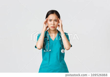 Covid-19, healthcare workers, pandemic concept. Overworked and exhausted asian female doctor, physician feeling sick, wear scrubs, touching head, complaining on headache or high fever Covid-19, healthcare workers, pandemic concept. Overworked and exhausted asian female doctor, physician feeling sick, wear scrubs, touching head, complaining on headache or high fever 109526868