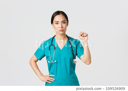 Covid-19, healthcare workers, pandemic concept. Serious-looking confident serious asian female doctor showing support to fellow collegues during coronavirus, raising fist in unity gesture Covid-19, healthcare workers, pandemic concept. Serious-looking confident serious asian female doctor showing support to fellow collegues during coronavirus, raising fist in unity gesture 109526909