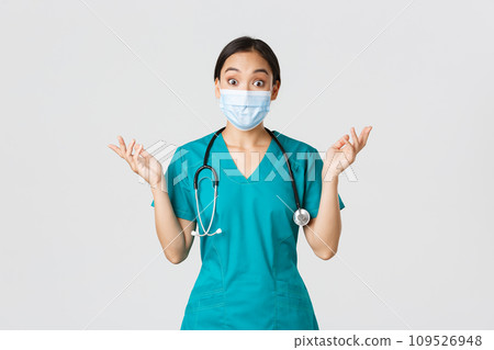 Covid-19, coronavirus disease, healthcare workers concept. Surprised and amazed asian female nurse, physician in medical mask and scrubs raising hands up excited, hear amazing news, white background 109526948