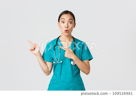 Covid-19, healthcare workers, pandemic concept. Impressed and amazed female asian nurse in scrubs asking question with intrigued expression. Doctor looking thrilled and pointing upper left corner Covid-19, healthcare workers, pandemic concept. Impressed and amazed female asian nurse in scrubs asking question with intrigued expression. Doctor looking thrilled and pointing upper left corner 109526981