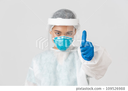 Covid-19, coronavirus disease, healthcare workers concept. Serious-looking confident asian female doctor, physician in personal protective equipment in respirator, show thumbs-up, white background 109526988