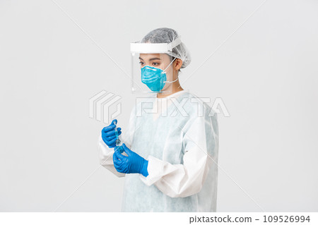 Covid-19, coronavirus disease, healthcare workers concept. Side view of serious young asian female doctor, physician in personal protective equipment insert syringe into ampoule with vaccine 109526994