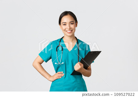 Healthcare workers, preventing virus, quarantine campaign concept. Smiling pleasant asian female physician, doctor during examination wearing scrubs and holding clipboard, white background Healthcare workers, preventing virus, quarantine campaign concept. Smiling pleasant asian female physician, doctor during examination wearing scrubs and holding clipboard, white background 109527022