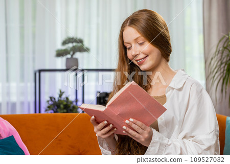 Teen girl relaxing interesting book turning pages smiling enjoying literature taking a rest on sofa 109527082