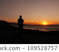 A man standing on the beach watching the sunset 109528757