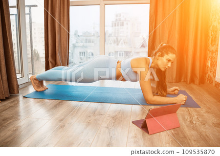 Young attractive athletic woman in blue sportswear doing push ups or pushups on gym mat at home, practicing yoga plank pose, exercising indoors, healthy active lifestyle concept Young attractive athletic woman in blue sportswear doing push ups or pushups on gym mat at home, practicing yoga plank pose, exercising indoors, healthy active lifestyle concept 109535870