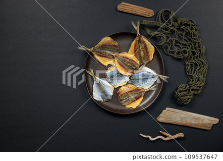 a plate of dried fish on a black background. Top view on a black background with an eco shopper. 109537647