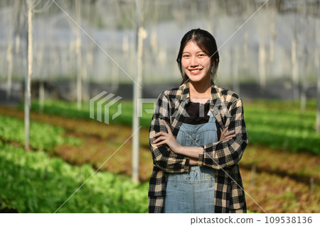 Portrait of cheerful female farmer standing with crossed arms at greenhouse of organic vegetables 109538136