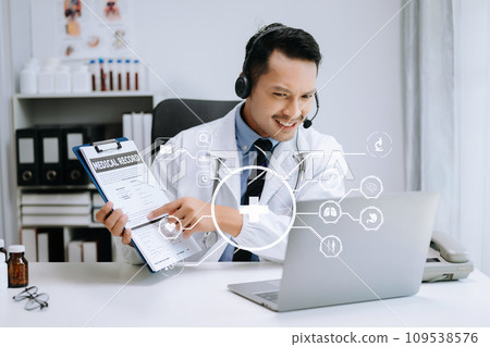 Attractive male doctor talking while explaining medical treatment to patient through a video call with laptop in office Attractive male doctor talking while explaining medical treatment to patient through a video call with laptop in office 109538576
