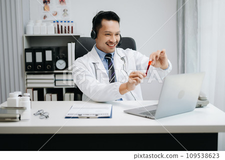 Attractive male doctor talking while explaining medical treatment to patient through a video call with laptop in office Attractive male doctor talking while explaining medical treatment to patient through a video call with laptop in office 109538623