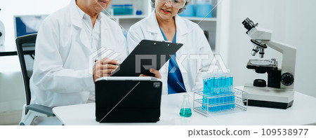 Two Senior scientists conducting research investigations in a medical laboratory, a researcher in the foreground is using a microscope in laboratory for medicine. . Two Senior scientists conducting research investigations in a medical laboratory, a researcher in the foreground is using a microscope in laboratory for medicine. . 109538977