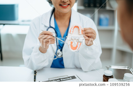 Concentrated dentist sitting at table with jaw samples tooth model and working with tablet and laptop in dental office professional dental clinic. medical doctor working . 109539256
