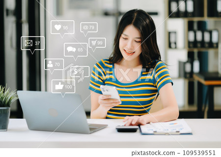Asian woman typing smartphone, keyboard with laptop computer of Social media and Marketing virtual icons screen concept. Asian woman typing smartphone, keyboard with laptop computer of Social media and Marketing virtual icons screen concept. 109539551