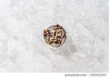 Flat lay. Homemade chocolate hazelnut fudge square pieces on a white plate. Flat lay. Homemade chocolate hazelnut fudge square pieces on a white plate. 109542347