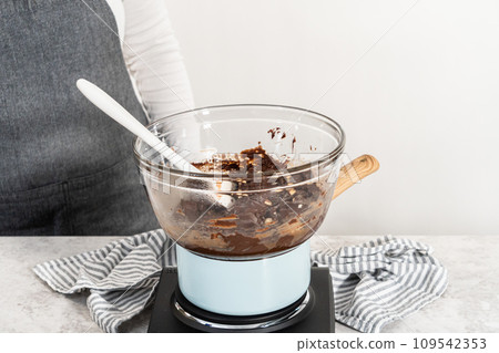 Melting chocolate chips and other ingredients in a glass mixing bowl over boiling water to prepare chocolate hazelnut fudge. Melting chocolate chips and other ingredients in a glass mixing bowl over boiling water to prepare chocolate hazelnut fudge. 109542353