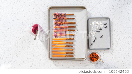 Flat lay. Dipping pretzel rods into melted chocolate to make Halloween chocolate-covered pretzel rods. Flat lay. Dipping pretzel rods into melted chocolate to make Halloween chocolate-covered pretzel rods. 109542463