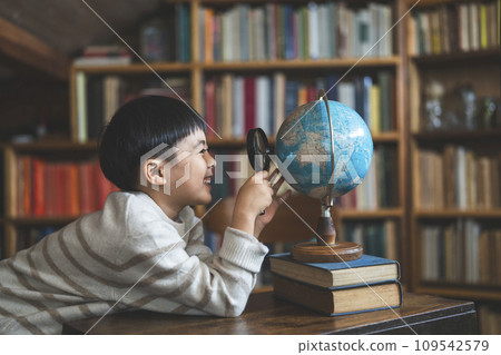 Smiling boy looking at the globe with a magnifying glass, profile 109542579