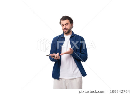 a young well-groomed brunette guy in a casual blue shirt holds a mobile phone in his hands and a young well-groomed brunette guy in a casual blue shirt holds a mobile phone in his hands and 109542764