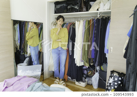 A young woman worries as she unfolds her clothes in front of her in the morning closet. A young woman worries as she unfolds her clothes in front of her in the morning closet. 109543993
