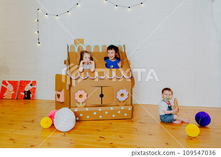 Joyful siblings running after each other and around cardboard house. 109547036