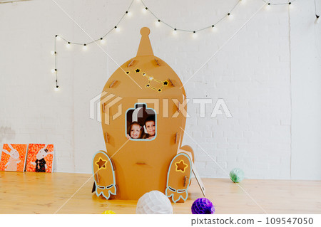 Joyful siblings running after each other and around cardboard rocket 109547050