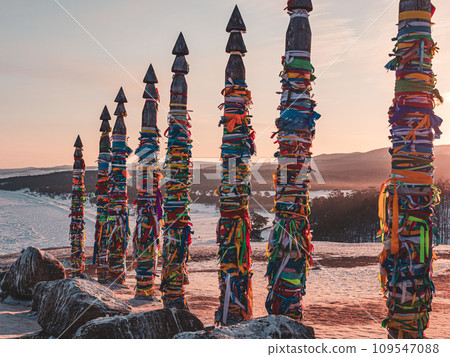 Traditional buryat shaman sacred pillars with colorful ribbons in winter at sunset, cape Burkhan, Olkhon island. Winter Baikal. Traditional buryat shaman sacred pillars with colorful ribbons in winter at sunset, cape Burkhan, Olkhon island. Winter Baikal. 109547088