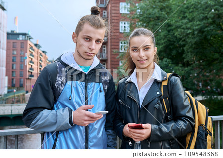 Outdoor portrait of teenagers students, smiling guy and girl with backpack looking at camera 109548368
