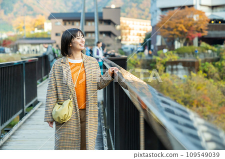 A woman crossing a bridge A woman standing in the autumn leaves 109549039