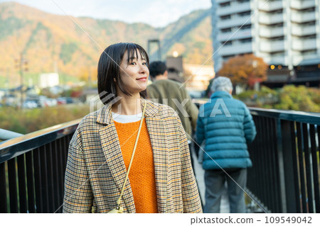 A woman crossing a bridge A woman standing in the autumn leaves 109549042