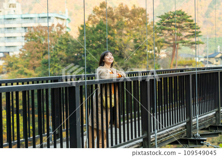 A woman crossing a bridge A woman standing in the autumn leaves 109549045