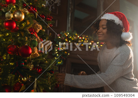 Merry Christmas. African American woman decorating Christmas tree. Happy girl near traditional Christmas tree with classical red golden decorations ornament. Christmas eve at home time for celebration 109549304
