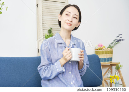 A middle-aged woman relaxing at home wearing pajamas and holding a mug 109550360