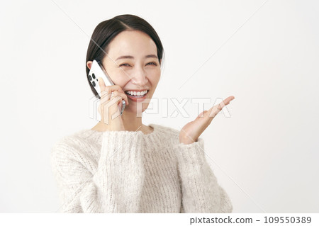 Middle-aged woman pointing to the right side with her palm while talking on a smartphone, white background Middle-aged woman pointing to the right side with her palm while talking on a smartphone, white background 109550389