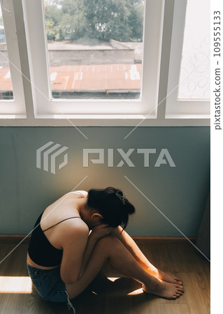 Thoughtful girl sitting on sill embracing knees looking at window, sad depressed teenager spending time alone at home, young upset pensive woman feeling lonely or frustrated thinking about problems Thoughtful girl sitting on sill embracing knees looking at window, sad depressed teenager spending time alone at home, young upset pensive woman feeling lonely or frustrated thinking about problems 109555133