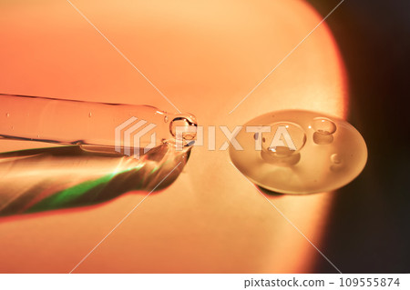 A dropper and a drop of sunscreen body serum in the orange sunset light. 109555874