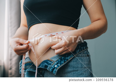 Close up of a belly with scar from c-section and abdominal fat. Women's health. A woman dressed up in sportswear demonstrating her imperfect body after a childbirth with nursery on the background. 109556178