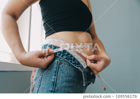 Close up of a belly with scar from c-section and abdominal fat. Women's health. A woman dressed up in sportswear demonstrating her imperfect body after a childbirth with nursery on the background. 109556179