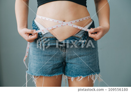 Close up of a belly with scar from c-section and abdominal fat. Women's health. A woman dressed up in sportswear demonstrating her imperfect body after a childbirth with nursery on the background. 109556180