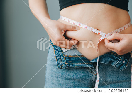 Close up of a belly with scar from c-section and abdominal fat. Women's health. A woman dressed up in sportswear demonstrating her imperfect body after a childbirth with nursery on the background. Close up of a belly with scar from c-section and abdominal fat. Women's health. A woman dressed up in sportswear demonstrating her imperfect body after a childbirth with nursery on the background. 109556181