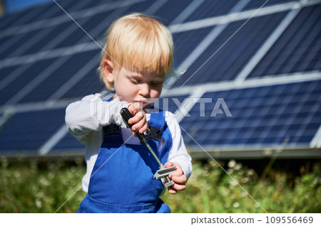 Little child learning how to use screwdriver on background of solar panels. Curious kid interested in repairing. Blond toddler tries to tighten the screw. 109556469