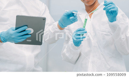 Man and woman use a test tube and a pipette while working in a greenhouse. 109558009
